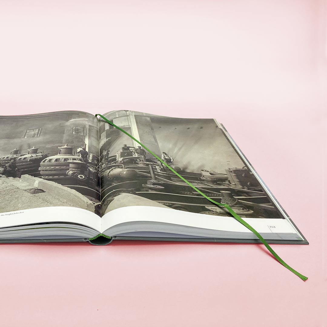 Aufgeklapptes Hardcoverbuch mit grünem Lesezeichen. Die Kathedrale des Walchenseekraftwerks zum Zeitpunkt der Fertigstellung.