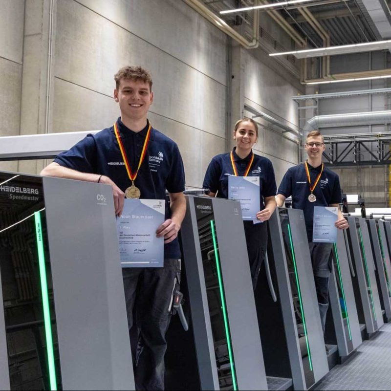 Gruppenfoto: die Deutsche Druckertechnik Meister:innen auf einer Druckmaschine